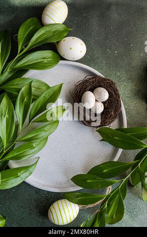 From above place setting for Easter dinner with ceramic plates easter eggs in nest surrounded by Italian ruscus leaves Stock Photo