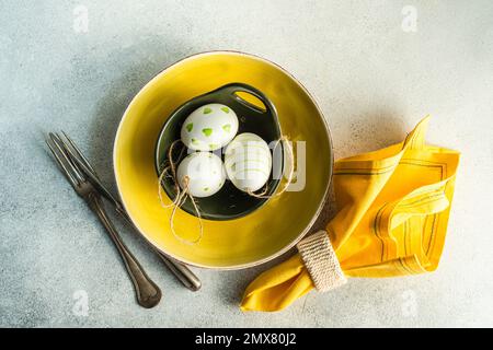 From above place setting for Easter dinner with yellow ceramic plate and bowl with easter eggs on concrete background Stock Photo