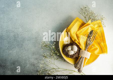 From above place setting for Easter dinner with yellow ceramic plates near nest with easter eggs surrounded by cushion baby's-breath leaves Stock Photo