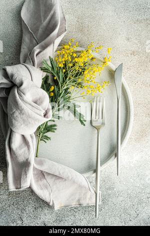 Festive table setting for Easter holiday dinner with bright yellow mimosa flowers on concrete table Stock Photo