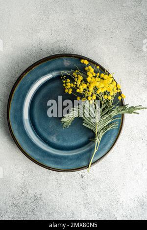 Festive table setting for Easter holiday dinner with bright yellow mimosa flowers on concrete table Stock Photo