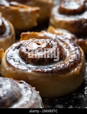 Appetizing baked sweet cinnamon rolls with white cream topping served on table in bakery Stock Photo