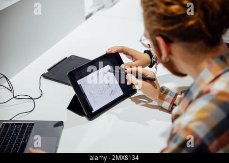 High angle of crop anonymous male pointing at tablet screen with pen while discussing new clothes with female colleague in modern office Stock Photo