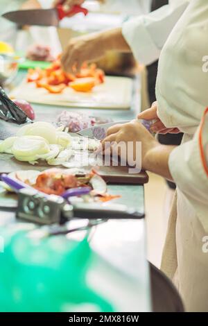 Side view of crop anonymous female cooks in uniform standing at counter cutting vegetables while preparing food in restaurant kitchen Stock Photo