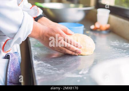 Side view of crop anonymous female chef in uniform kneading soft dough on table with flour in kitchen Stock Photo