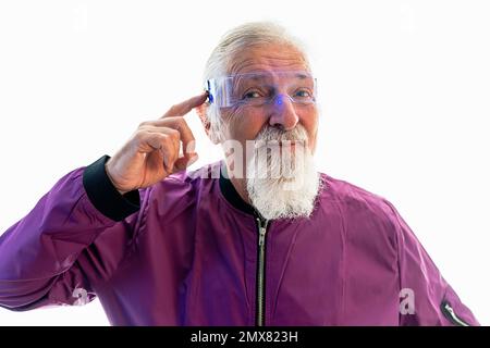 Portrait of senior bearded male hipster in glasses and bright jacket looking at camera while pointing at head against white background Stock Photo