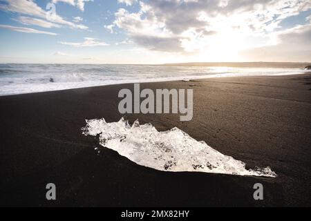 Selective focus of transparent piece of ice melting in sunlight on seacoast of black sandy beach in Iceland Stock Photo