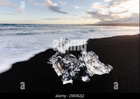 Selective focus of transparent piece of ice melting in sunlight on seacoast of black sandy beach in Iceland Stock Photo