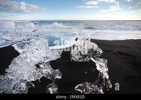 Selective focus of transparent piece of ice melting in sunlight on seacoast of black sandy beach in Iceland Stock Photo