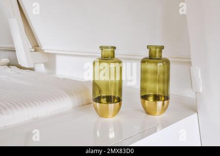 Glass green transparent vases with golden elements placed on white table in light room Stock Photo