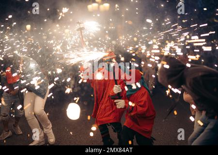 Anonymous people in bright festive clothes standing on street with burning sparklers during city celebration Stock Photo