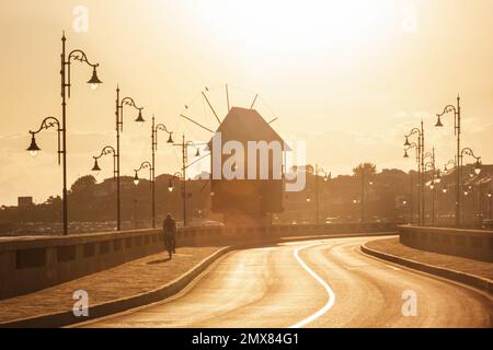 Morning city landscape - view of the road with the wooden windmill before the entrance to the Old Town of Nessebar, on the Black Sea coast of Bulgaria Stock Photo