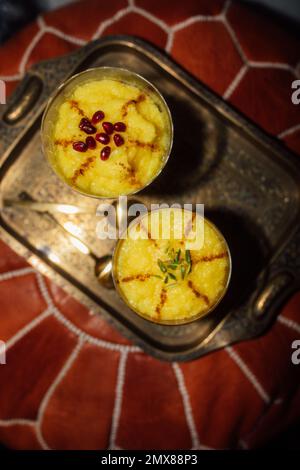 two servings of Sholeh Zard, a Persian saffron rice pudding, dessert with cinnamon, pomegranate and pistachio garnish Stock Photo