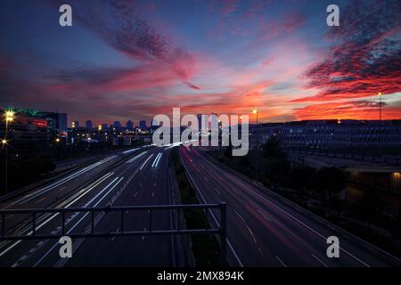 View of the city skyline at sunset with a glare on a bridge and traces of light from the headlights of cars Stock Photo