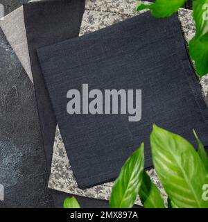 Folded black napkins on black background with green leaves. Eco friendly Mock up for display or montage of dishes, food or washing detergent. Showcase Stock Photo