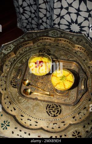 two servings of Sholeh Zard, a Persian saffron rice pudding, dessert with cinnamon, pomegranate and pistachio garnish Stock Photo