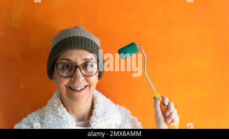 Middle aged woman painting a wall. Portrait of smiling woman holding a roller brush. Moving house. Selective focus included. Noise and grain included Stock Photo