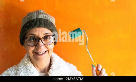 Middle aged woman painting a wall. Portrait of smiling woman holding a roller brush. Moving house. Selective focus included. Noise and grain included Stock Photo