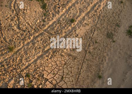 High resolution top-down view of cracked dry desert earth with tire tracks running across at sunset. Stock Photo