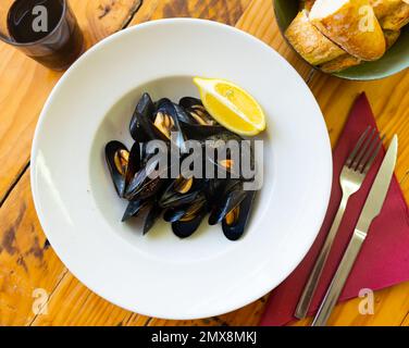 Baked mussels in shells on plate with slice of lemon Stock Photo