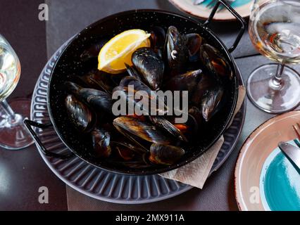 Steamed mussels in shells with lemon in metal serving pan Stock Photo