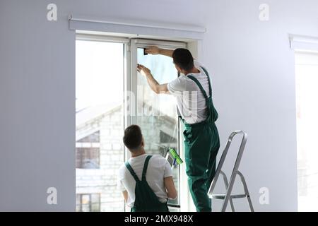 Professional workers tinting window with foil indoors Stock Photo