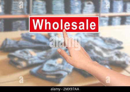 Woman clicking Wholesale button and blurred view of shop with stylish jeans on background Stock Photo