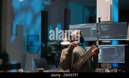 Careless html coder playing air guitar with keyboard, having fun and acting silly after hours. IT engineer fooling around with instrument and enjoying late night working in office, happy man. Stock Photo