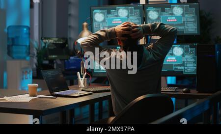Frustrated hacker using computer to break into corporate data servers, working under pressure. Infecting software system with dangerous network virus, stealing security information. Tripod shot. Stock Photo