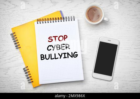 Notebooks with phrase STOP CYBER BULLYING and cup of coffee on wooden table, flat lay Stock Photo