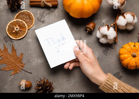Woman holding paper sheet with text THANK YOU and autumn decor on dark background Stock Photo