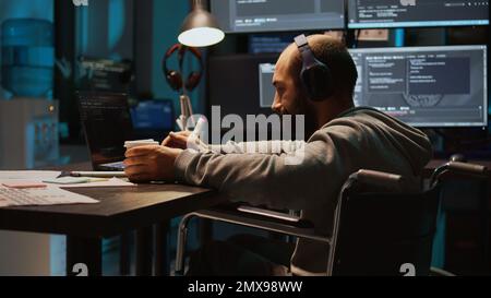 Software engineer using terminal window on laptop to program new code, dealing with physical impairment. Male web developer in wheelchair coding firewall security or html script. Handheld shot. Stock Photo