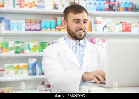 Professional pharmacist working on laptop in modern drugstore Stock Photo