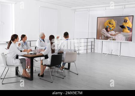 Team of doctors using video projector during coronavirus conference in office Stock Photo