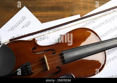 Beautiful violin, bow and note sheets on wooden table, flat lay Stock Photo