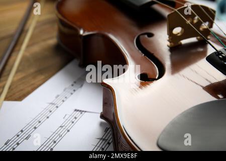 Beautiful violin, bow and note sheets on wooden table, closeup Stock Photo