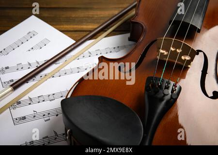 Beautiful violin, bow and note sheets on wooden table, closeup Stock Photo