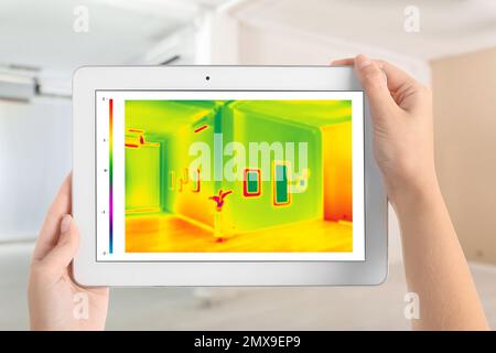 Woman detecting heat loss in room using thermal viewer on tablet. Energy efficiency Stock Photo