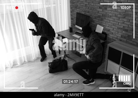 Dangerous masked criminals with weapon stealing money from house, view through CCTV camera Stock Photo