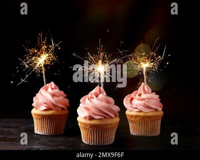 Birthday cupcakes with sparklers on table against dark background Stock Photo