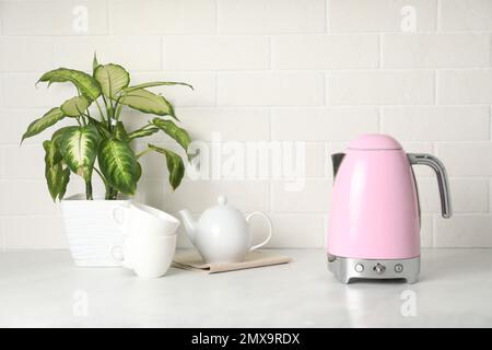 Modern electric kettle, houseplant and tea set on counter in kitchen Stock Photo