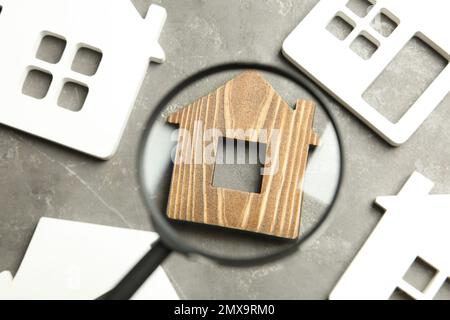 Magnifying glass and house models on grey stone table. Search concept Stock Photo