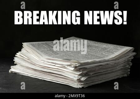 Phrase Breaking News and stack of newspapers on dark stone table. Journalist's work Stock Photo