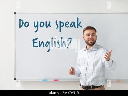 Young English teacher near whiteboard in classroom Stock Photo