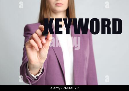 Woman writing word KEYWORD on transparent board against grey background, closeup Stock Photo