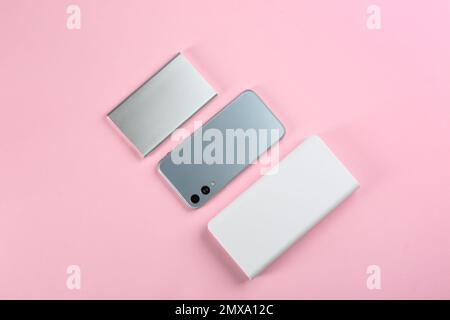 Mobile phone and portable chargers on pink background, flat lay Stock Photo