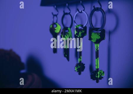 Holder with different keys on wall, view under UV light. Sanitizing objects during coronavirus outbreak Stock Photo