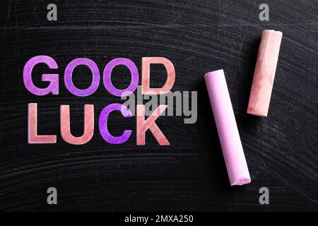 Pieces of color chalk and phrase GOOD LUCK on blackboard, flat lay Stock Photo