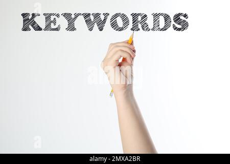 Woman writing word KEYWORDS on transparent board against white background, closeup Stock Photo