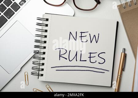 Notebook with text NEW RULES, laptop and pen on white table, flat lay Stock Photo